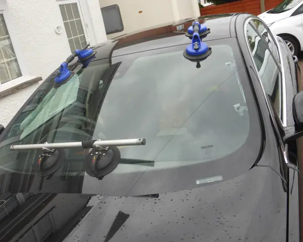 Suction cups on a new windshield being fitted to a car in a driveway